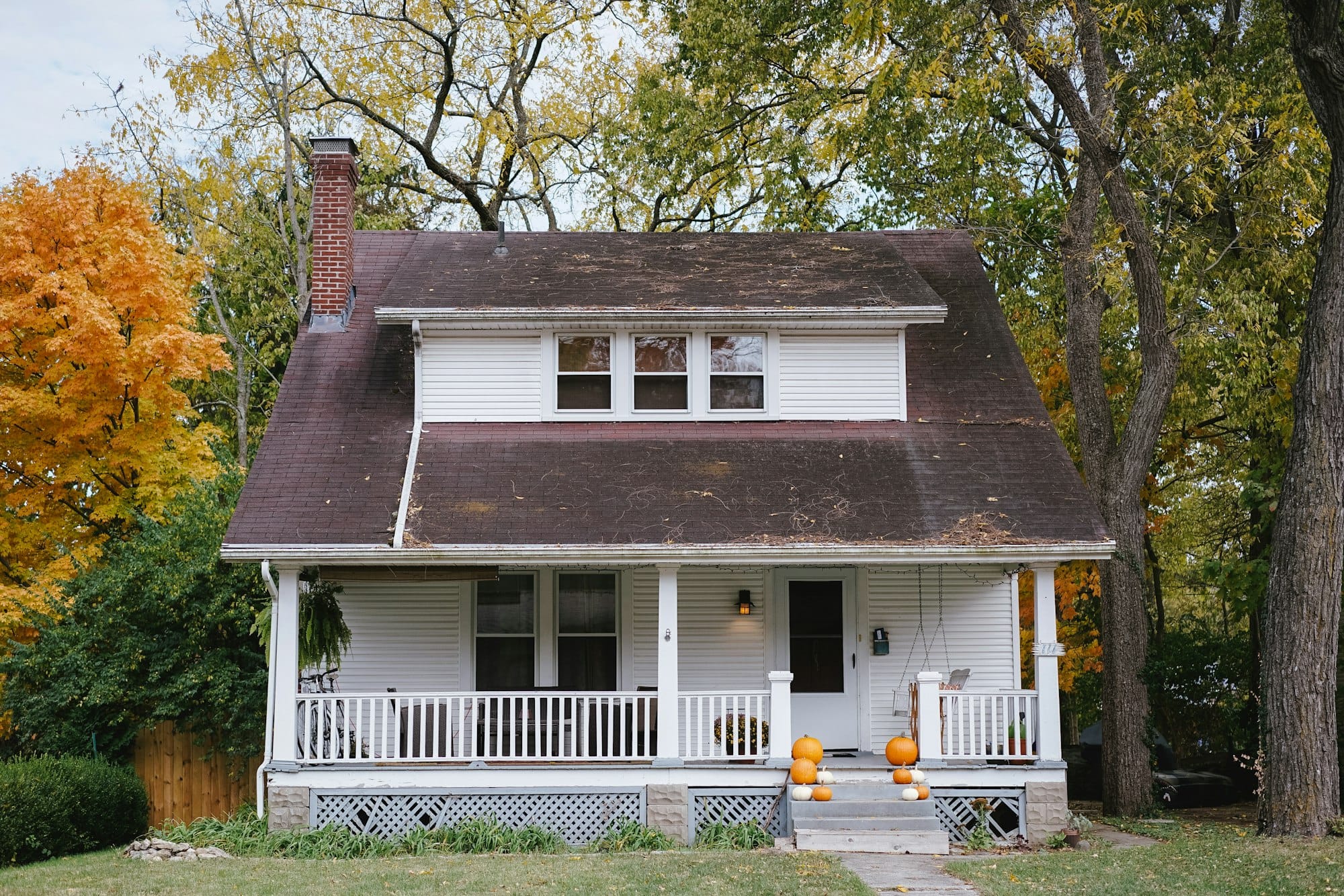 A white cottage with a front porch under autumn trees