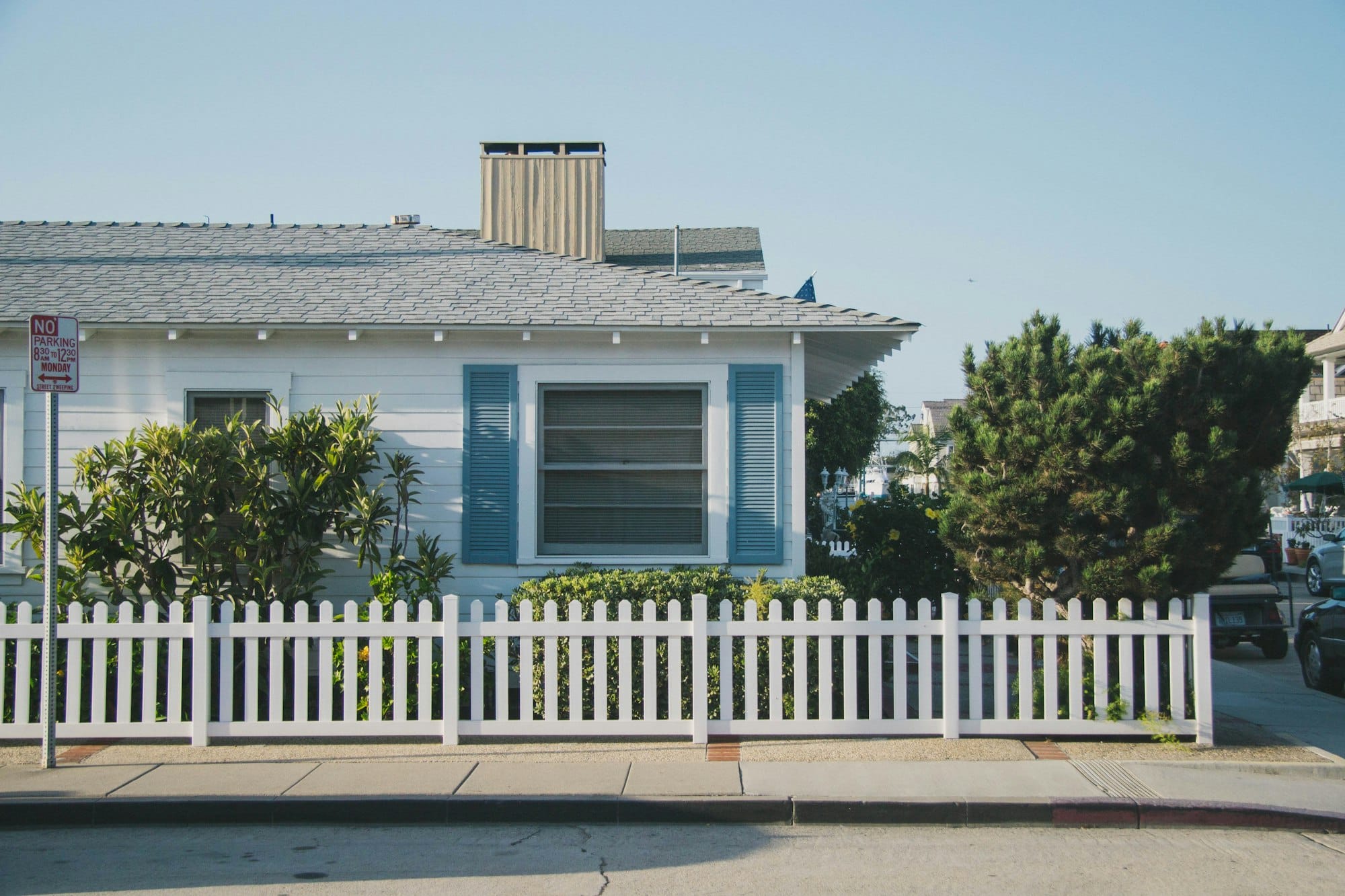 A white cottage with blue shutters behind a white picket fence